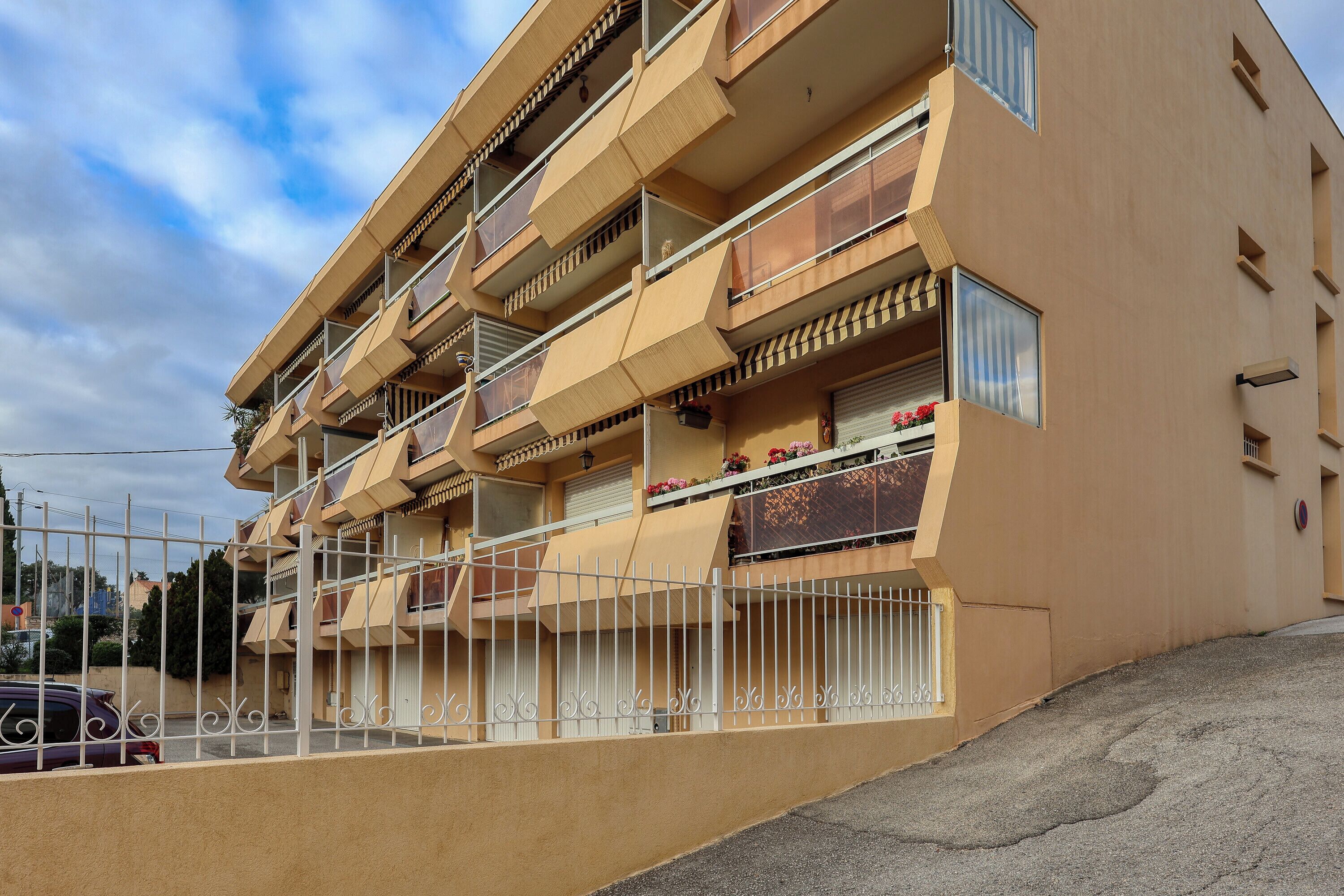 A multi-story residential building with balconies, a gated entrance, and a clear sky.