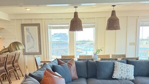 Una sala moderna con un sofá modular, sillas de mimbre, una mesa de centro y ventanas amplias que ofrecen vistas al exterior.