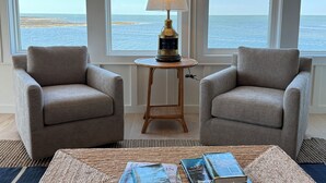 Una habitación con dos sillones, una mesita con lámpara y vistas al mar a través de amplios ventanales.