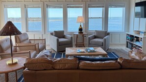 Una sala de estar con vista al mar, un ventilador de techo y una estantería.