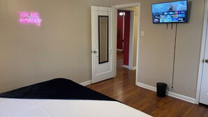 A bedroom with a bed, a neon sign, a television, and a hallway leading to another room.