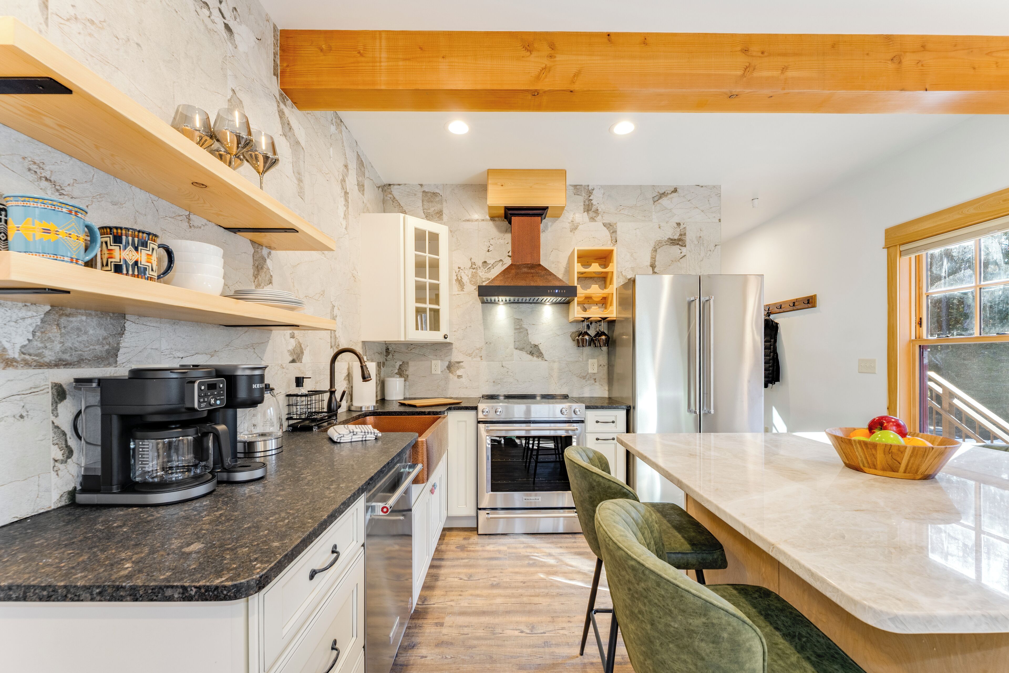 Une cuisine moderne dotée de plans de travail en granit, d’appareils électroménagers en acier inoxydable et de poutres en bois.