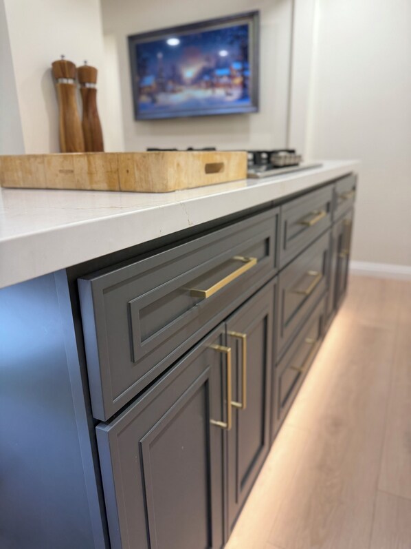 Cozinha com armários escuros, bancada branca e tábua de corte de madeira.