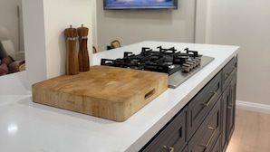 A modern kitchen with a central island, a gas stove, a stainless steel range hood, and a painting of a snowy village on the wall.