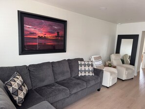 A living room with a grey sofa, a framed sunset picture, and a white armchair.