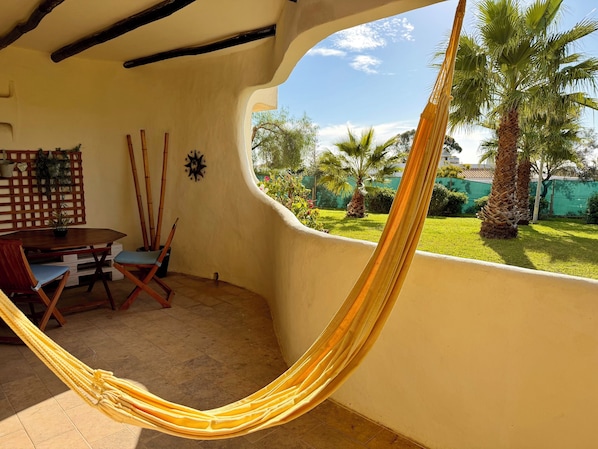 A hammock in a room with a view of a garden and palm trees. - Adorable Condo - Patio - Garden View - AC/Heating - WiFi-9 min Walk to Beach (Carvoeiro)