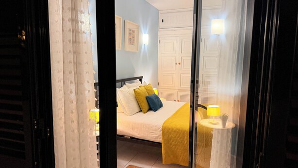 Quarto com cama, luminárias de cabeceira, guarda-roupa e espelho.