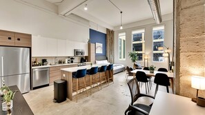 A modern kitchen with a central island, bar stools, and a dining area with a table and chairs. - Downtown Dallas Gem - 1000Mbps Fiber, Free Valet & Pool (Dallas)