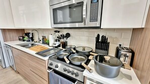 A modern kitchen with stainless steel appliances, a microwave, a stove, and various pots and pans. - Downtown Dallas Gem - 1000Mbps Fiber, Free Valet & Pool (Dallas)