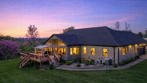 Une maison à deux étages dotée d’une terrasse et d’un porche couvert, entourée d’une pelouse bien entretenue et d’arbres.