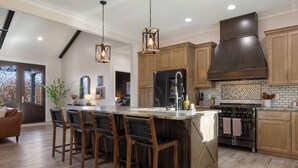 Une cuisine spacieuse dotée d’un grand îlot central, de tabourets de bar en bois, d’un réfrigérateur en acier inoxydable et d’une cuisinière moderne.