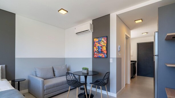 A modern hotel room with a grey sofa, a small round table, two chairs, a colorful abstract painting, and an air conditioning unit. - Studio 150m From Jurere Beach Pte0507 (Florianópolis)