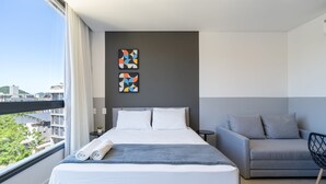 A modern hotel room with a large bed, a grey sofa, and two abstract paintings on the wall. - Studio 150m From Jurere Beach Pte0507 (Florianópolis)