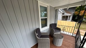 Een overdekt terras met twee rieten stoelen en een kleine ronde tafel.