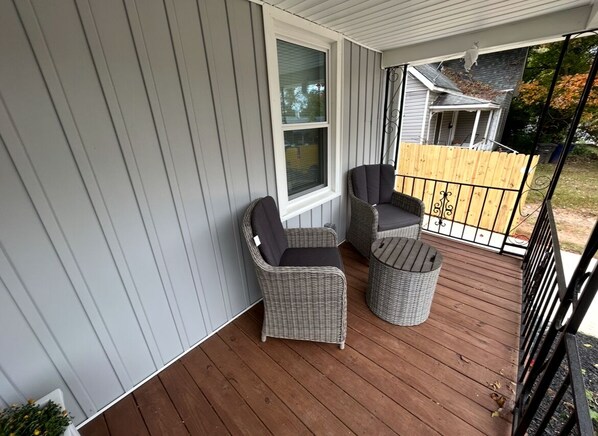 A covered porch with two wicker chairs and a small round table.