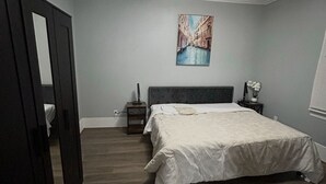 Een slaapkamer met een bed, een plafondventilator, een nachtkastje, een lamp en een schilderij aan de muur.