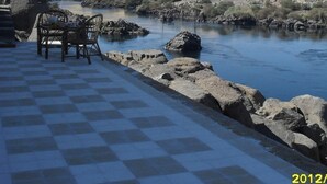 Un área de estar al aire libre con piso a cuadros y vistas a un río y colinas desérticas.