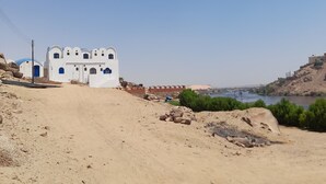 Un paisaje desértico con un edificio blanco con ventanas azules y un camino de tierra que lleva a él.