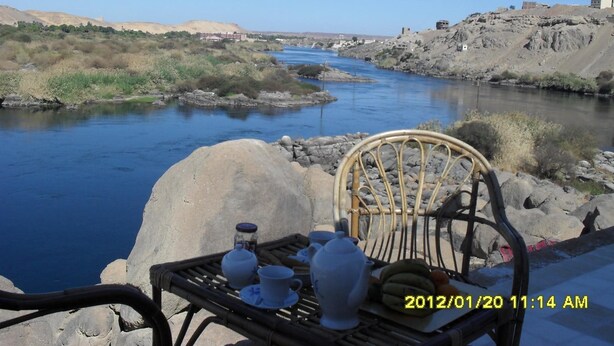 Una mesa con juego de té y comida, con vista a un río y edificios al fondo.