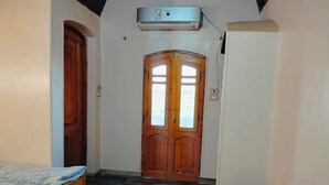 Un dormitorio con una cama de madera, una mesita de noche pequeña, un armario y un doble ventanal.