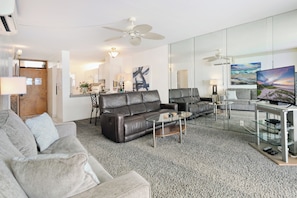 A modern living room with a leather sofa, a glass coffee table, and a flat-screen TV on a stand. - Oceanfront and beach front - Menehune Shores 411 (Kihei)