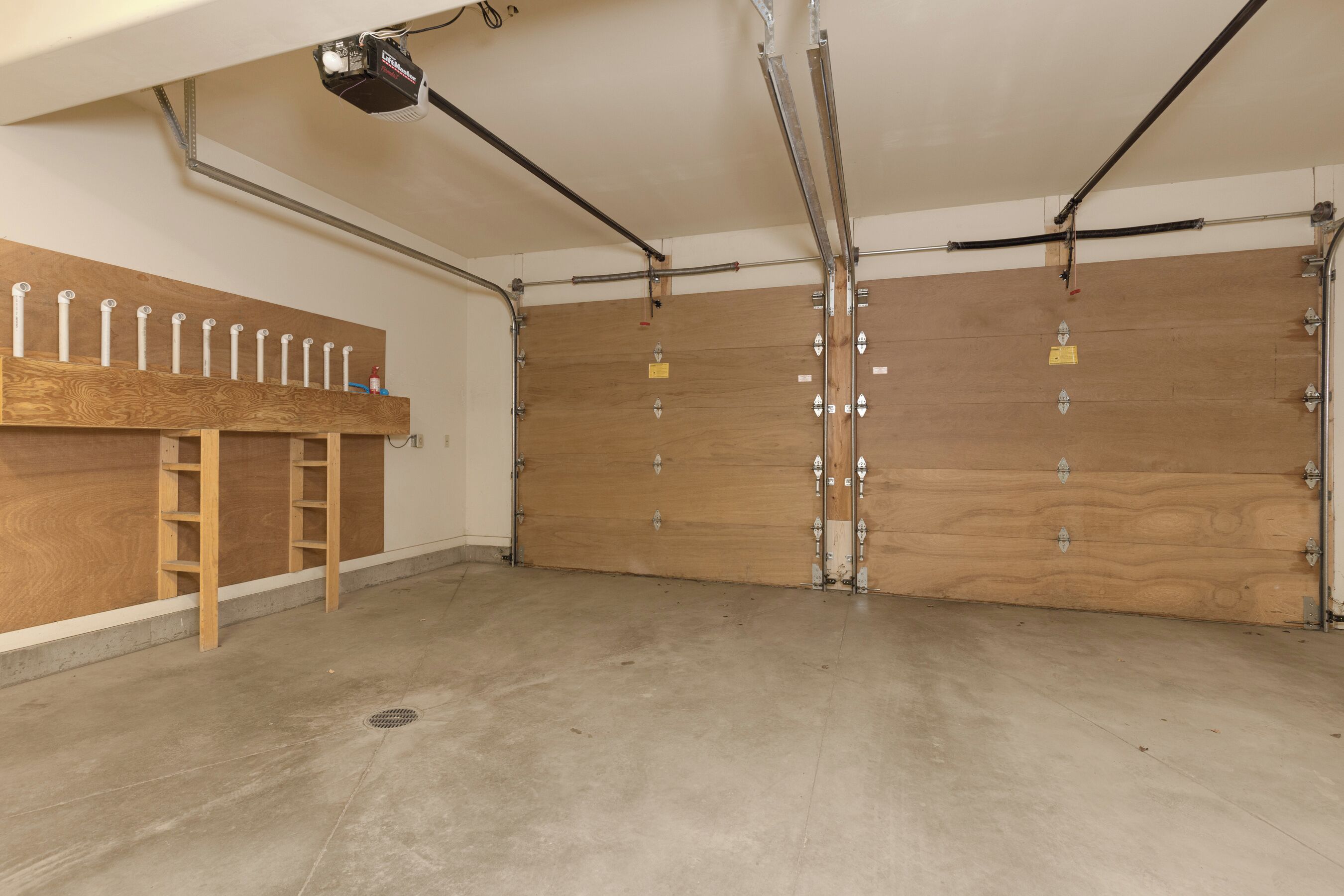 A garage with two wooden doors, a metal ladder, and a ceiling-mounted light fixture.