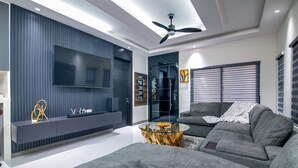 Ein modernes Wohnzimmer mit einem grauen Ecksofa, einem Glastisch und einem Flachbildfernseher, der an einer dunklen Wand angebracht ist.