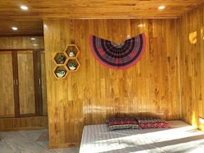 A wooden-paneled room with a bed, a decorative wall hanging, and hexagonal shelves with plants.