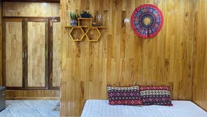 A wooden-paneled room with a bed, a decorative wall hanging, and a shelf with plants.