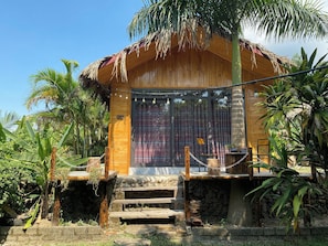 Une structure en bois surmontée d’un toit de chaume, entourée d’une végétation tropicale.