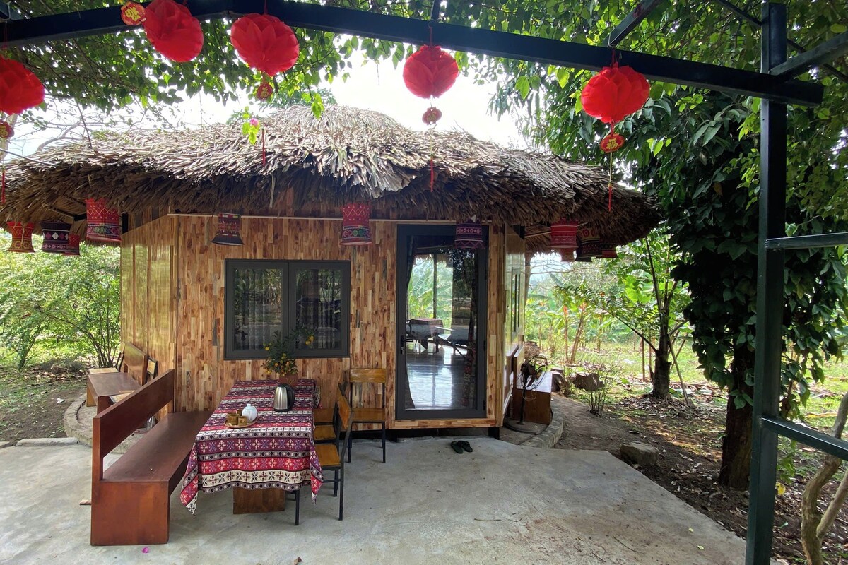 A rustic wooden structure with a thatched roof, a table with benches, and a door leading outside.