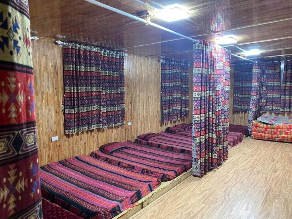 Een kamer met meerdere bedden, overdekt met beddengoed met een patroon, houten wanden en een houten vloer.