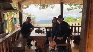 A wooden outdoor seating area with a table, benches, and a view of mountains in the background.