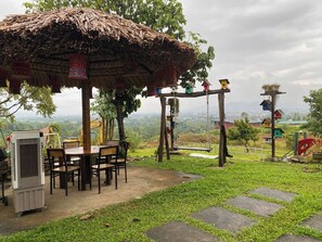 Un kiosque avec un toit de chaume, une table avec des chaises et un petit climatiseur.