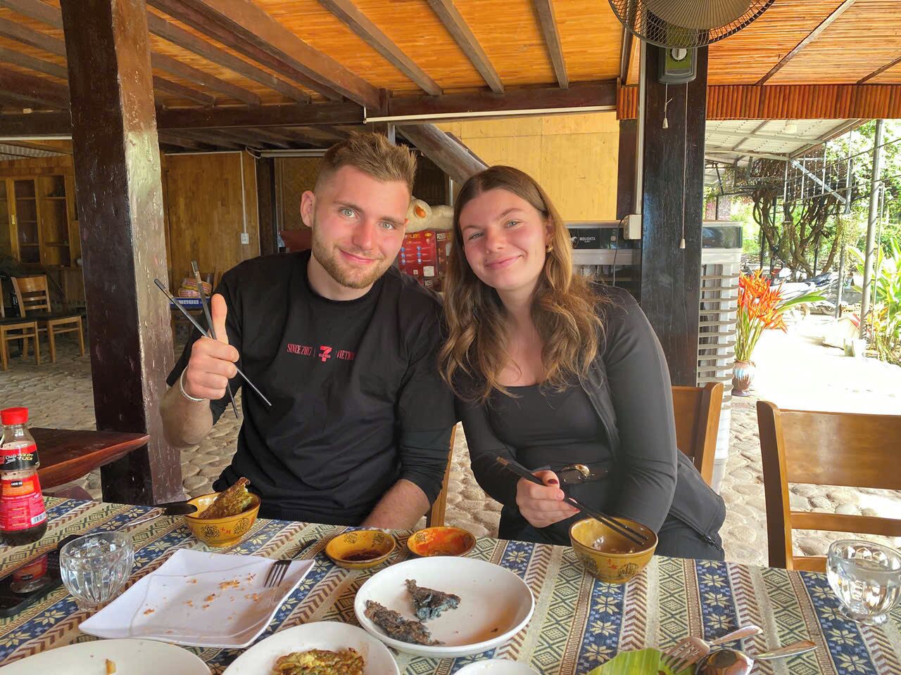 Two people dining at an outdoor table with various dishes and condiments.