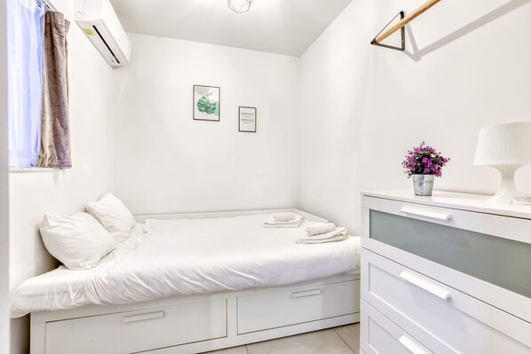 A small, white, single-bed room with a bedside table, a lamp, and a framed picture on the wall. - Central Msida Modern Bright Comfortable (Msida)