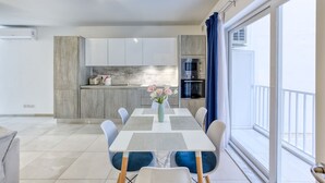 Een moderne keuken met witte kastjes, een ingebouwde magnetron en een eethoek met een tafel en stoelen.