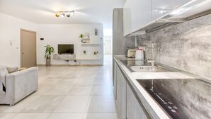 Een moderne keuken met een ingebouwde kookplaat, een spoelbak en een aanrecht. In de aangrenzende woonkamer staat een bank en een televisie.