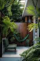 Un espacio al aire libre cubierto con una hamaca, una silla verde y abundante vegetación.