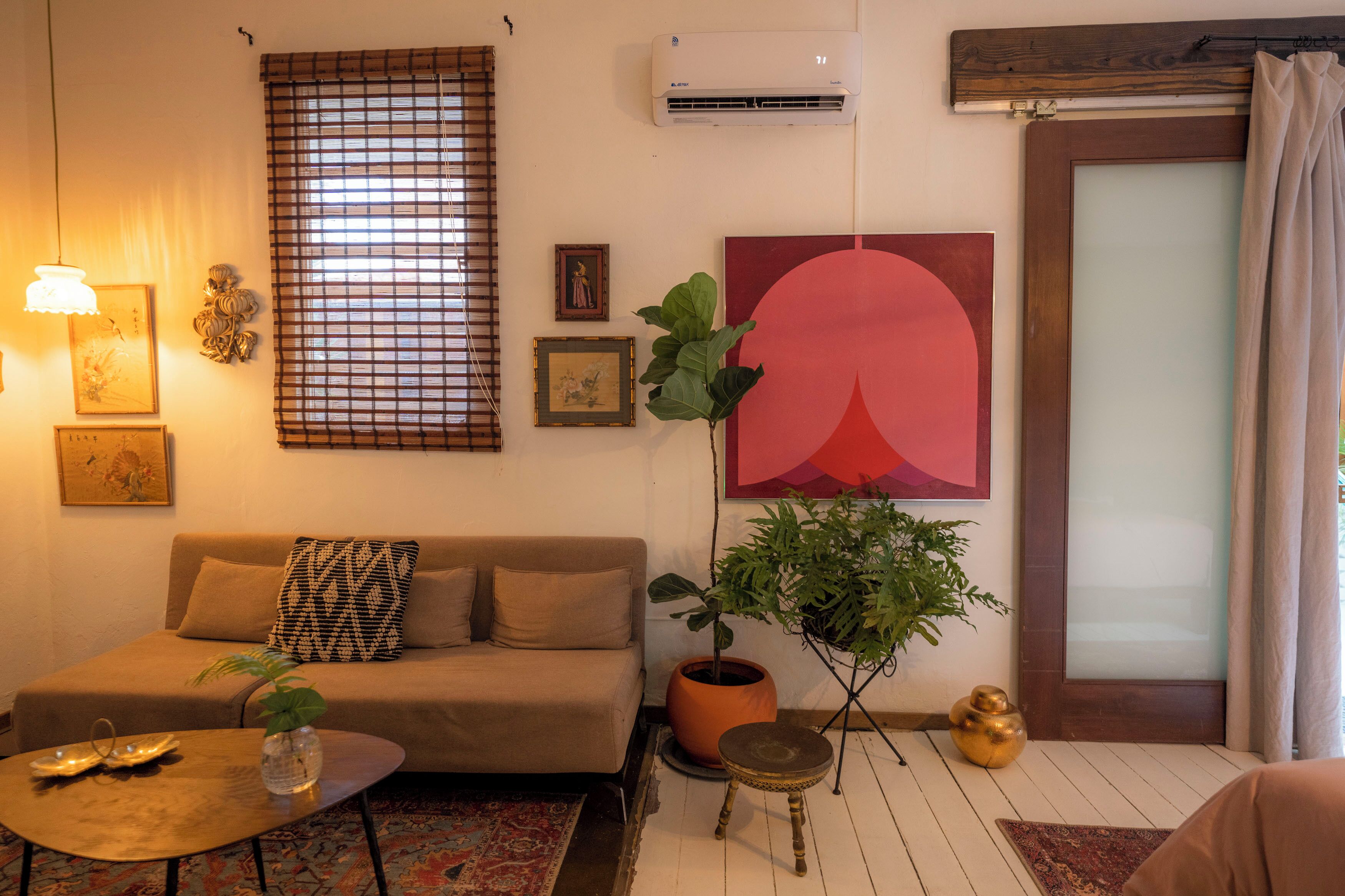 A living room with a sofa, a coffee table, a potted plant, and a large abstract painting.