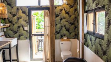 A room with a wooden ceiling, a black chair, a striped rug, a sink, and a toilet with a fern wallpaper.