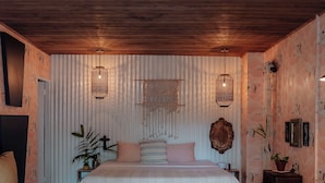 Un dormitorio con cama, mesitas de noche, lámpara colgante, sofá azul y alfombra estampada.