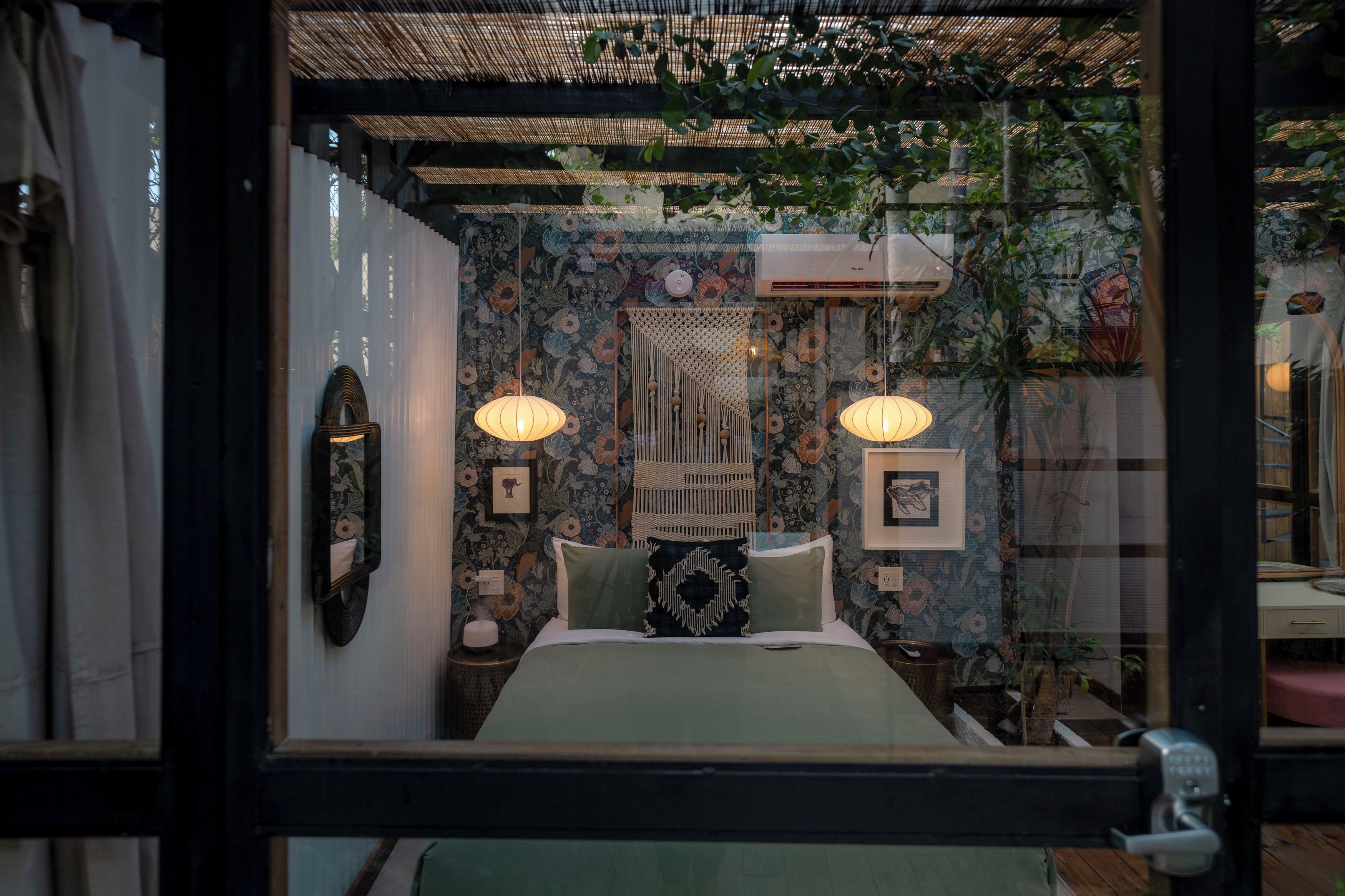 Una habitación con una cama, dos lámparas de pared, un muro decorativo y una ventana con vistas a la vegetación exterior.
