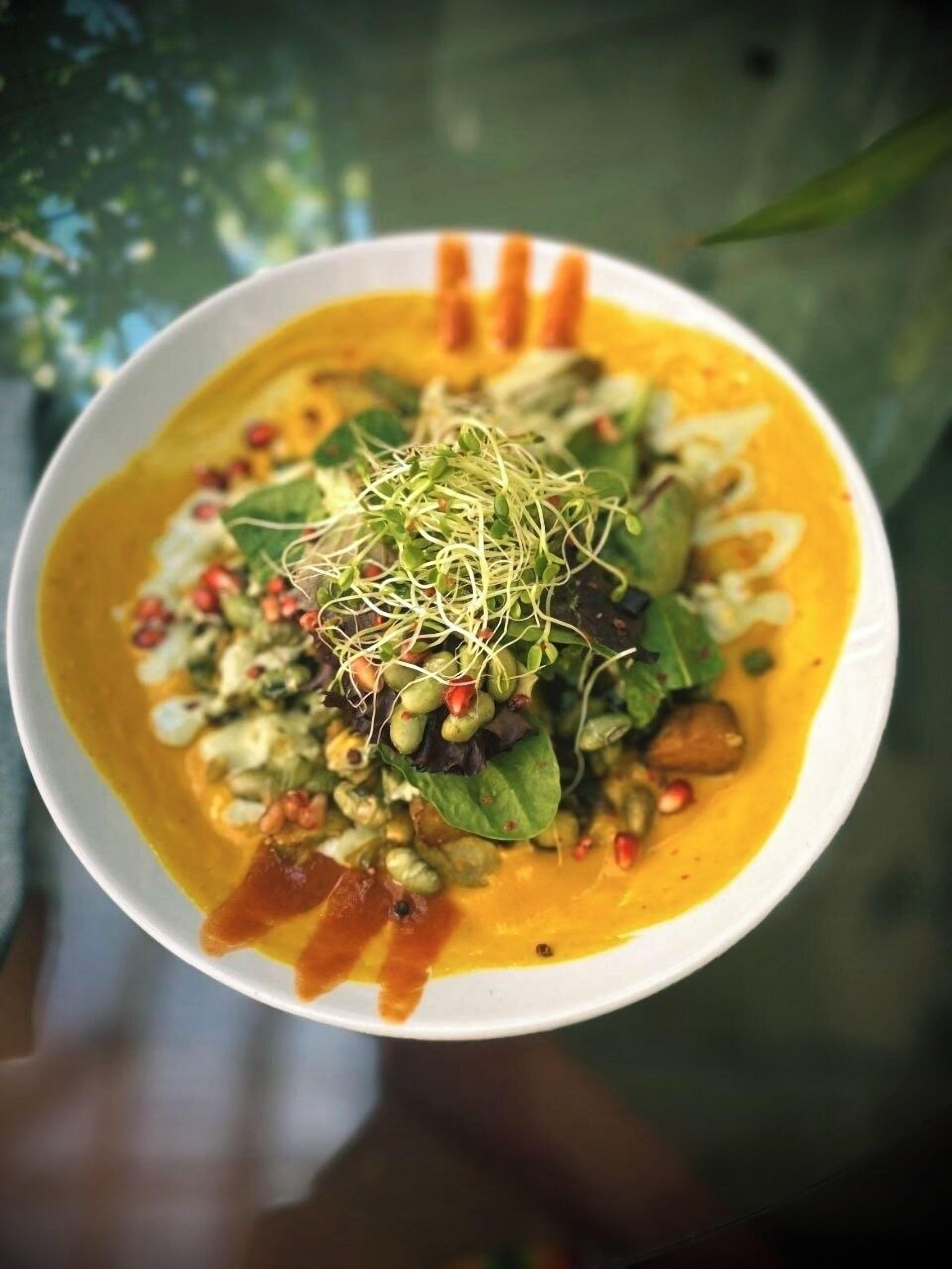 A bowl of soup with a garnish of sprouts and seeds, served in a white bowl.