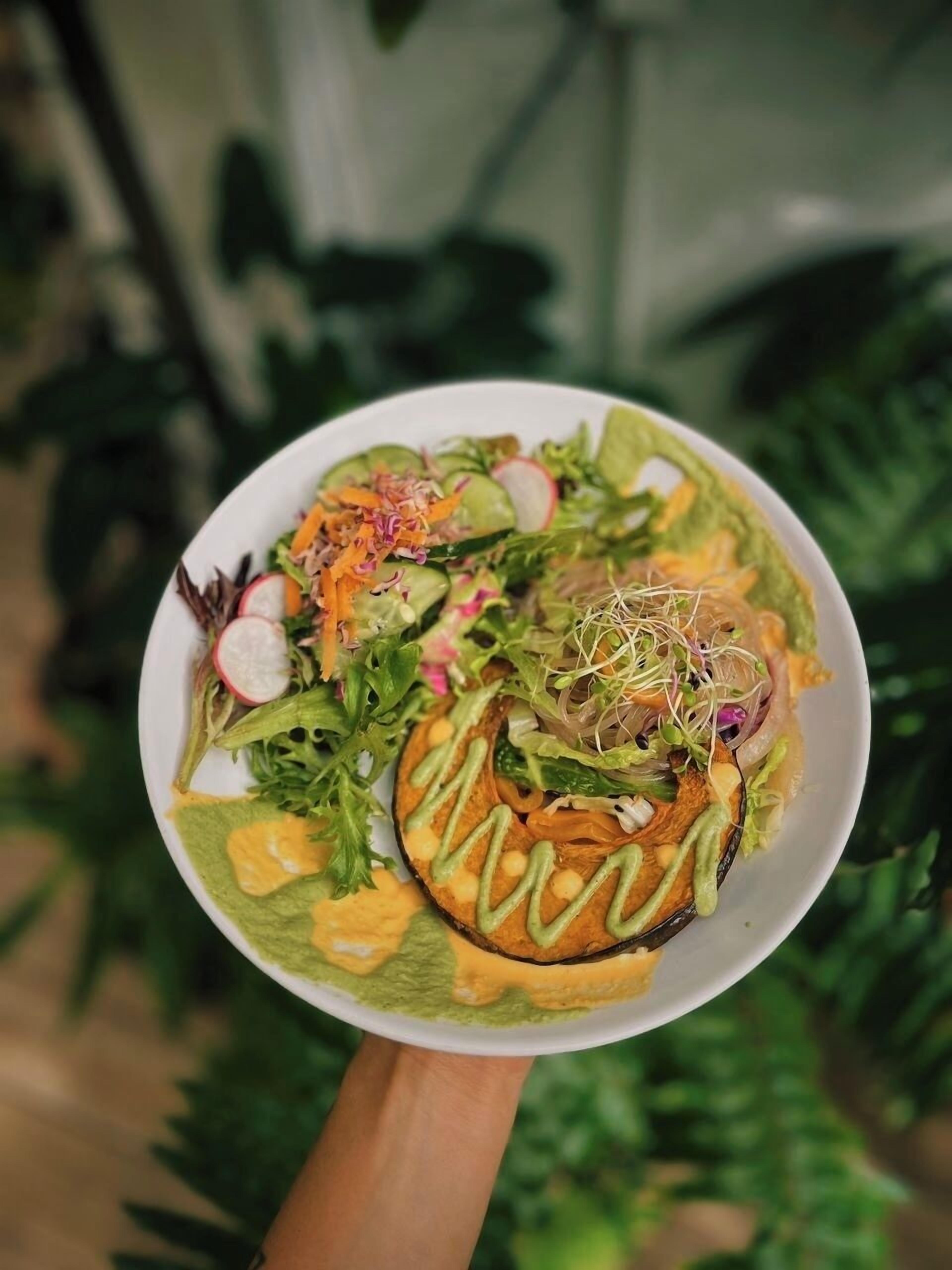 A bowl of salad with various vegetables and sprouts, held by a person.