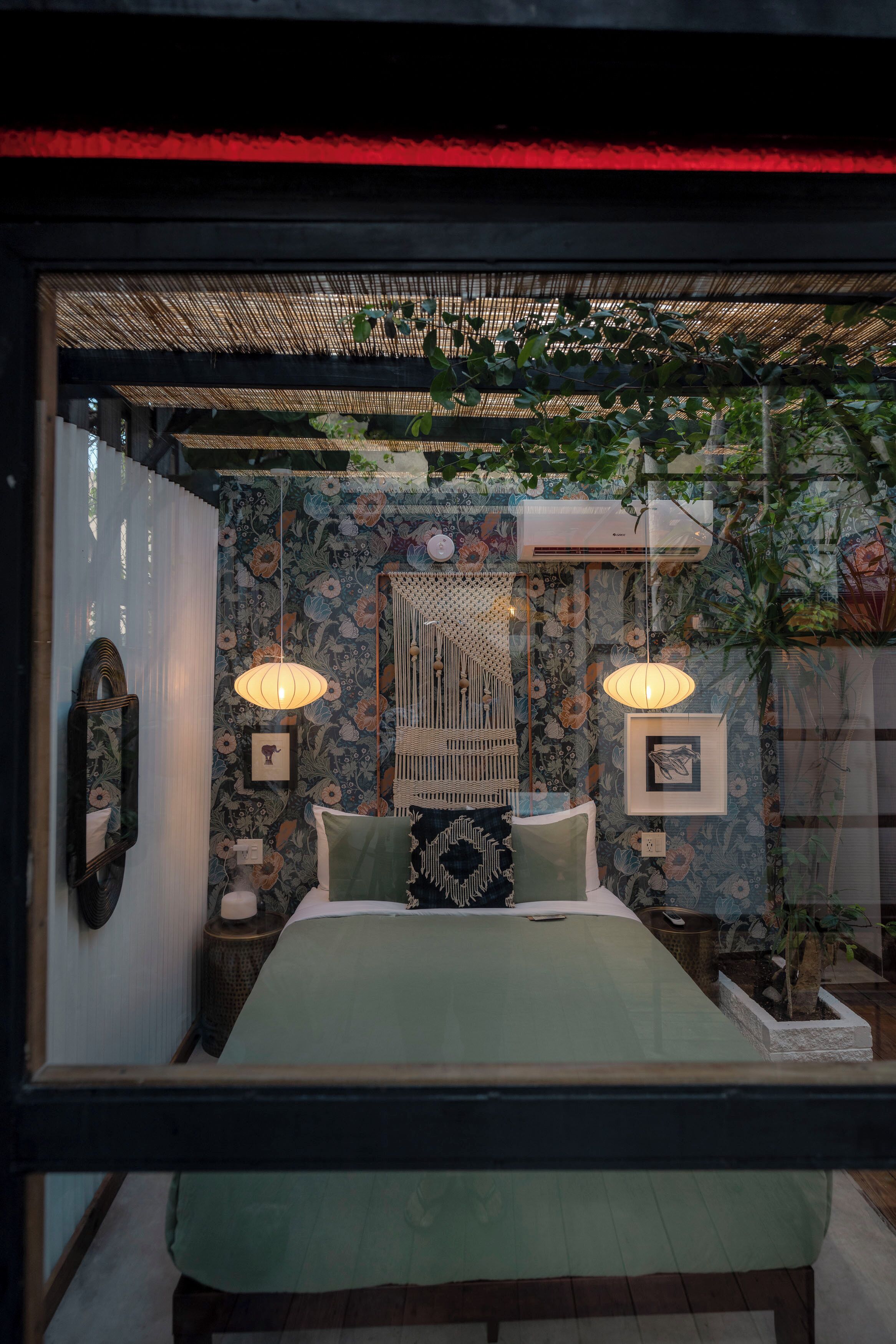 Une chambre à coucher comprenant un lit, des tables de chevet, des œuvres d’art murales et une fenêtre donnant sur un paysage verdoyant.