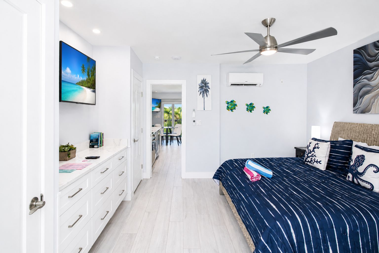 Ein Schlafzimmer mit Bett, Deckenventilator, Fernseher und Blick auf einen Essbereich.