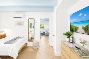 Habitación de hotel con cama, espejo, televisión y vista a la playa desde la ventana.