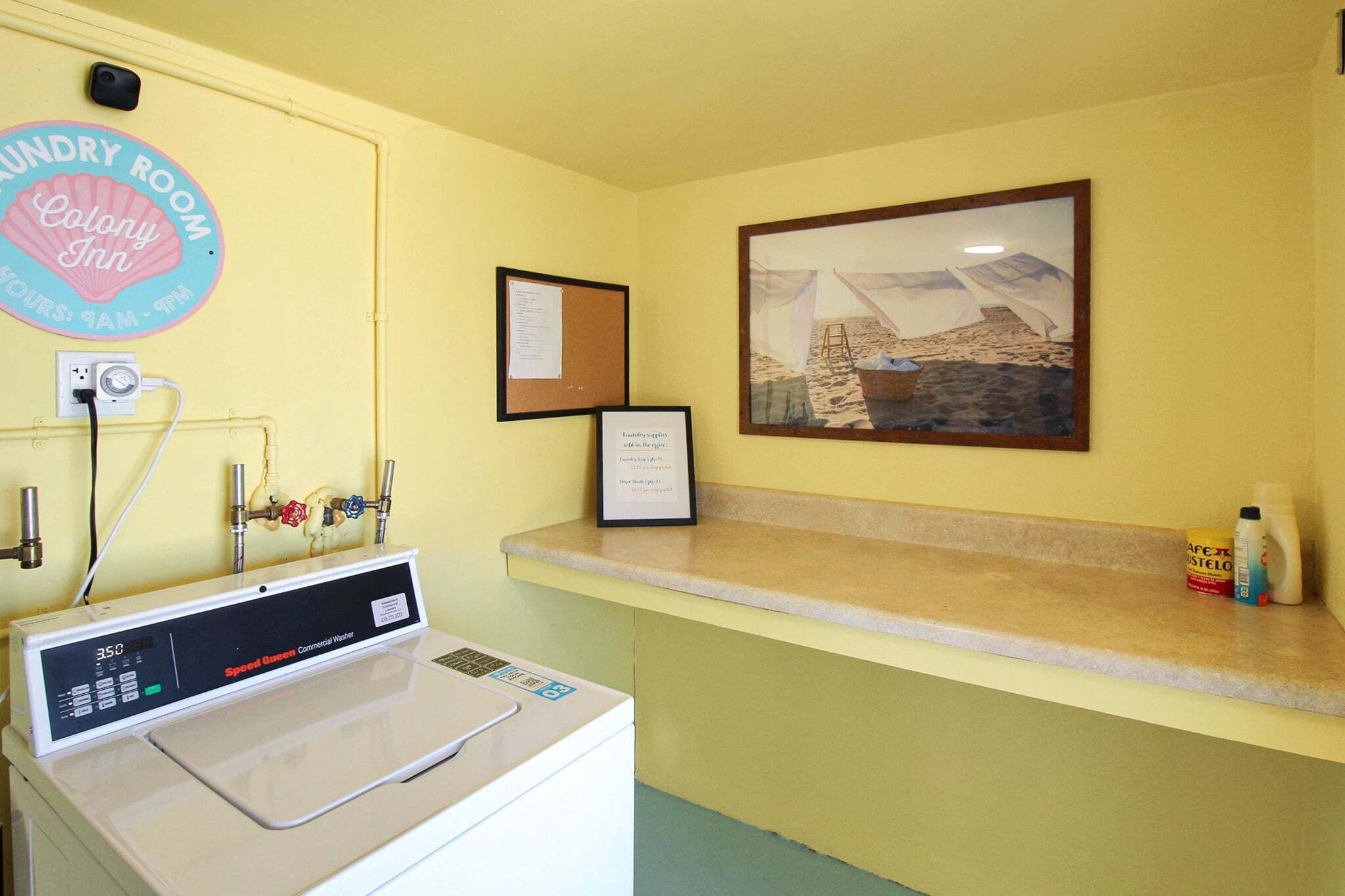 A laundry room with a washing machine, a sign for the Colony Inn, and a framed picture on the wall.