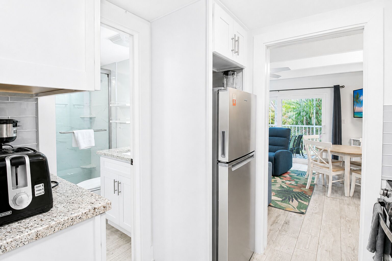 A modern kitchen with a built-in coffee maker, a refrigerator, and a glass shower enclosure.